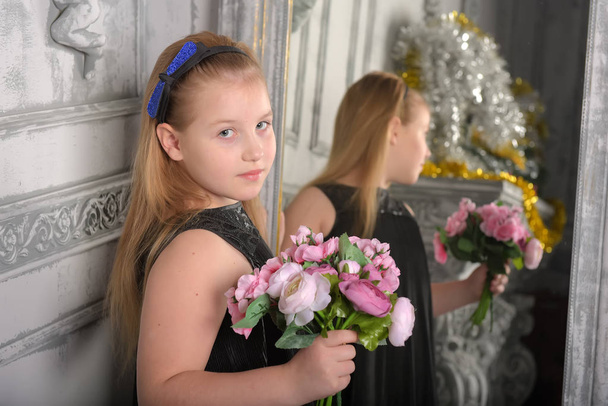 girl blonde child in a black dress with a bouquet in hand and a mirror - Фото, изображение