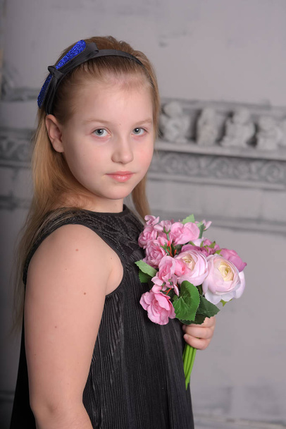 girl blonde child in a black dress with a bouquet in hand - 写真・画像