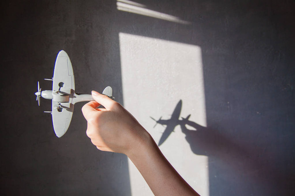 Interessante fundo abstrato com uma sombra na parede de concreto das cortinas. Uma mão está segurando um avião e há uma sombra na parede
. - Foto, Imagem