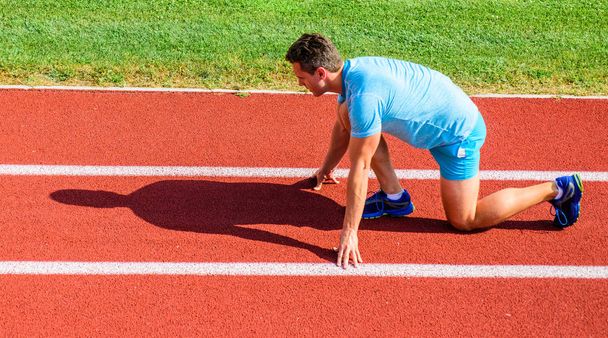 Hoe te beginnen te lopen. Sport motivatie concept. Man atleet runner stand laag start positie stadion pad zonnige dag. Loper klaar om te gaan. Inspannen voor de overwinning. Volwassen runner bereiden race stadium - Foto, afbeelding