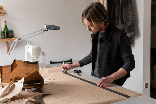 Young creative man tailor draws clothing pattern in workshop - Valokuva, kuva