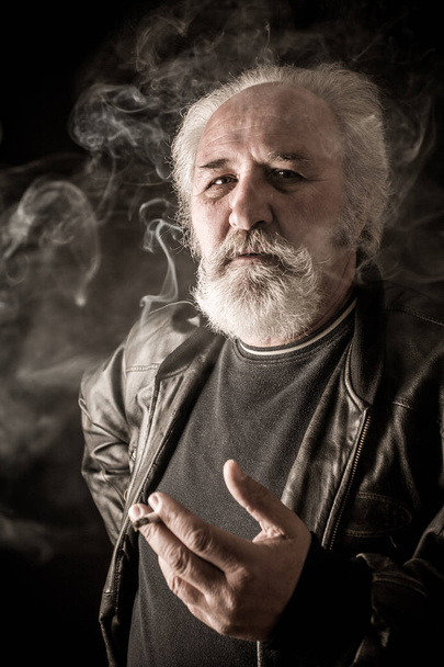 Грубий старший чоловік курить сигарету на темному тлі
 - Фото, зображення