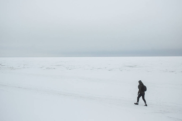 Alone man hiker with backpack going on winter sea coast. Minimalistic composition - Φωτογραφία, εικόνα