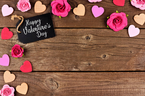 Happy Valentines Day hoekrand met cadeau label, houten hartjes en papieren rozen tegen een rustieke houten achtergrond. Kopiëren van ruimte. - Foto, afbeelding