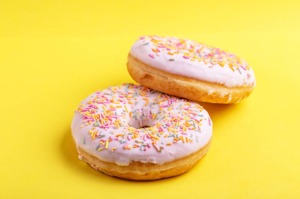 Two delicious vanilla donuts with sprinkle on bright yellow background. Unhealthy, but tasty sweets. Copy space. Top view - Foto, immagini
