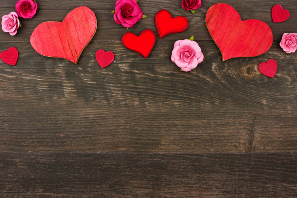 Valentines Day top border of wooden hearts and paper flowers against a dark wood background. Copy space. - Photo, Image
