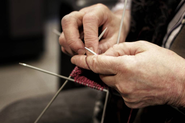 The hands of an elderly woman knit clothes out of wool yarn with knitting needles - Fotó, kép