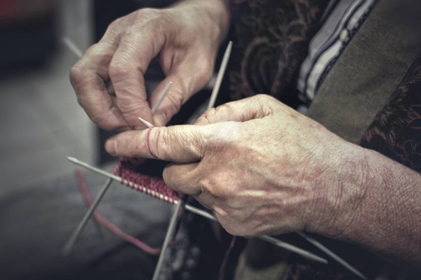 The hands of an elderly woman knit clothes out of wool yarn with knitting needles - Foto, imagen