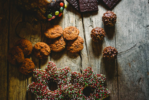 Pretty composition with warm light of Christmas sweets and chocolate cookies, festive background arranged on a rustic wooden table - Foto, afbeelding