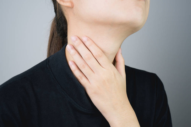 Primo piano delle mani delle donne stanno toccando il collo a causa del dolore a causa della malattia, uno sfondo grigio dà luce morbida
. - Foto, immagini