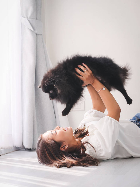 Szczęśliwy Asian kobieta, leżąc na podłodze i dotykając jej czarny pies z okna koncepcja oświetlenia, styl życia. - Zdjęcie, obraz