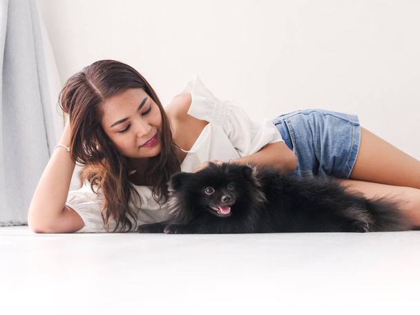 Happy Asian woman lying on floor and touching her black dog with window light, lifestyle concept. - Фото, зображення