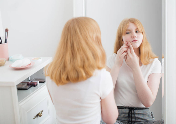 teen girl examines acne on face in front of mirror - Foto, immagini