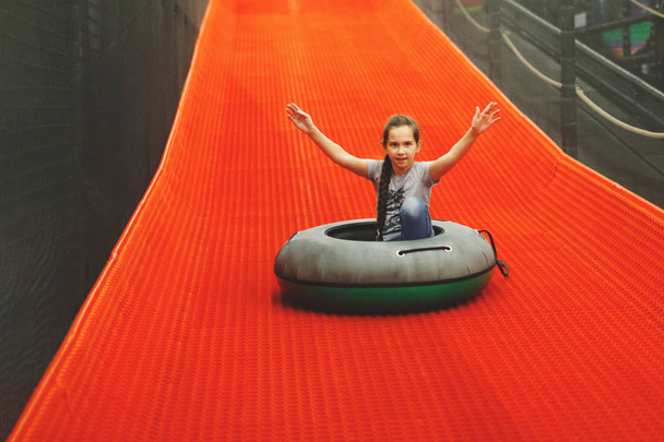 Teen girl rolls on an inflatable ring on an artificial hill in the children's center. - Photo, Image