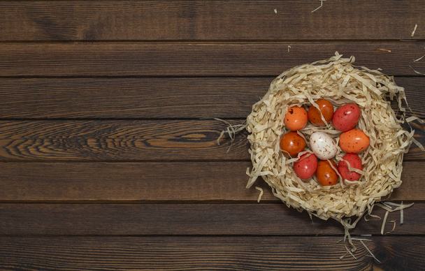 Colorful Easter egg in the nest on wood background. Top view with copy space - Valokuva, kuva