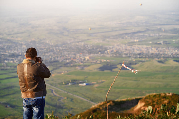 Traveller photographing mountain village and hot air balloons - Photo, Image