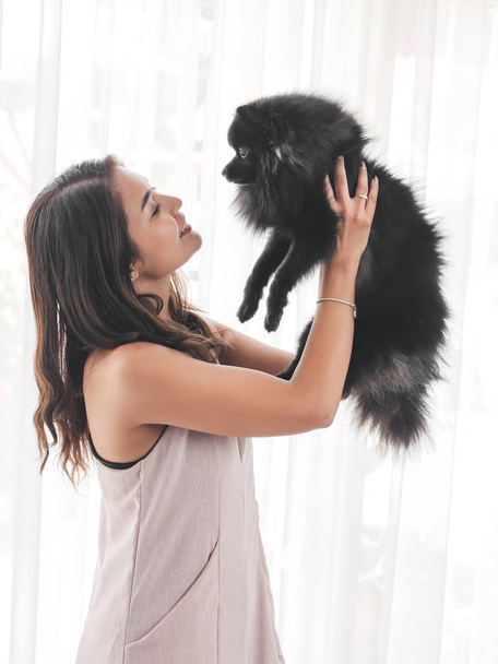 Happy Asian woman holding black dog near window at home. - Foto, afbeelding