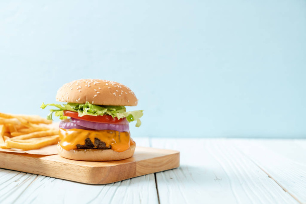 fresh tasty beef burger with cheese and french fries on wood background - 写真・画像