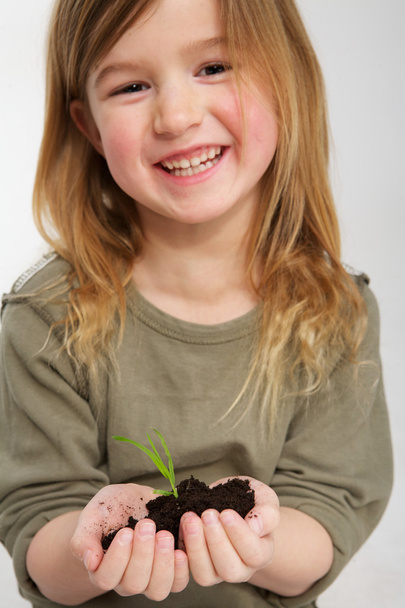 χαμογελαστό κορίτσι με το φυτό αυξάνεται από το χώμα στα χέρια - Φωτογραφία, εικόνα