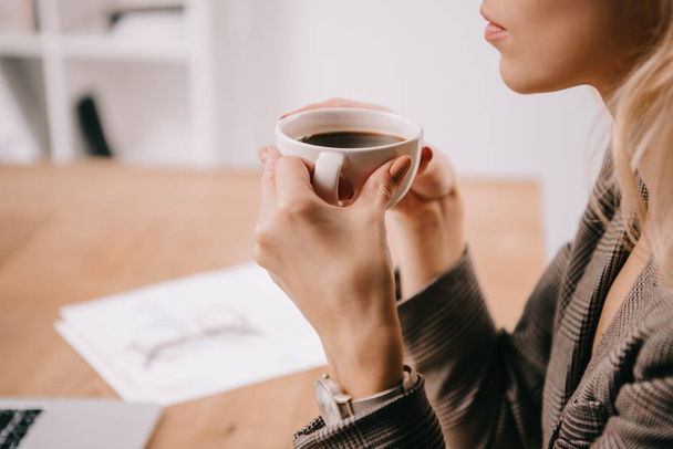 vista recortada de la mujer de negocios sosteniendo la taza de café en el descanso en la oficina
 - Foto, imagen
