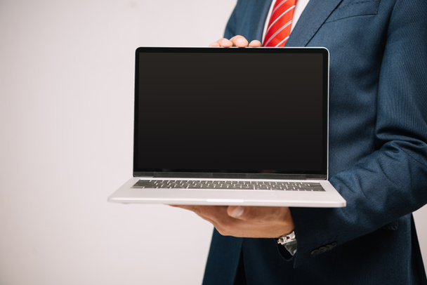 cropped view of businessman in suit presenting laptop with blank screen isolated on grey - Photo, Image