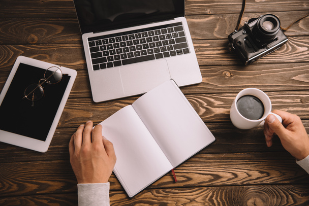 обрезанный вид блогера с ноутбуком, чашкой кофе, цифровыми устройствами и ретро фотокамерой
 - Фото, изображение