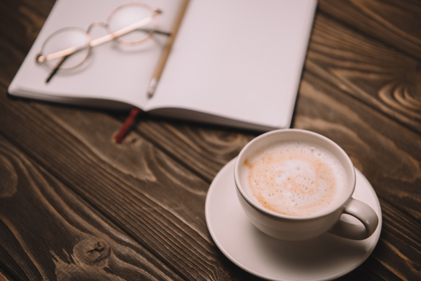 close up of cappuccino, notebook and eyeglasses on wooden table - Photo, Image