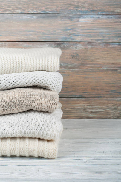 Knitted wool sweaters. Pile of knitted winter clothes on wooden background, sweaters, knitwear, space for text - Foto, Imagem