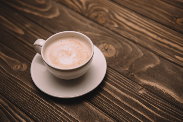 white saucer and cup with cappuccino on wooden table - Foto, immagini