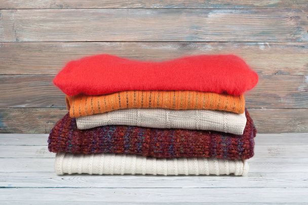 Knitted wool sweaters. Pile of knitted winter clothes on wooden background, sweaters, knitwear, space for text - Photo, image