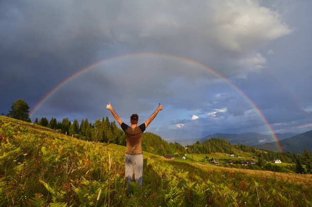 un giovane ragazzo, un turista, alzò le mani e i pollici verso l'alto, rallegrandosi dell'arcobaleno visto
 - Foto, immagini