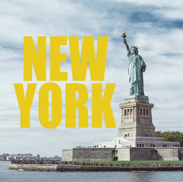 STATUE OF LIBERTY, NEW YORK, USA - OCTOBER 8, 2018: statue of liberty in new york against blue cloudy sky background with yellow "new york" lettering, usa - Foto, imagen