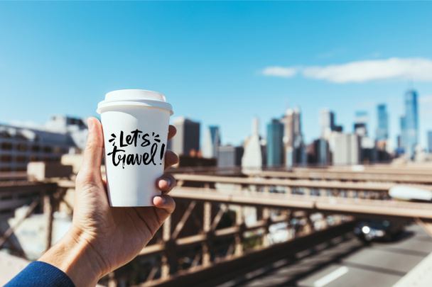 ember, aki eldobható csésze kávét egy részleges kilátás "lehetővé teszi, hogy utazási" betűkkel és homályos new Yorkban, a háttér - Fotó, kép
