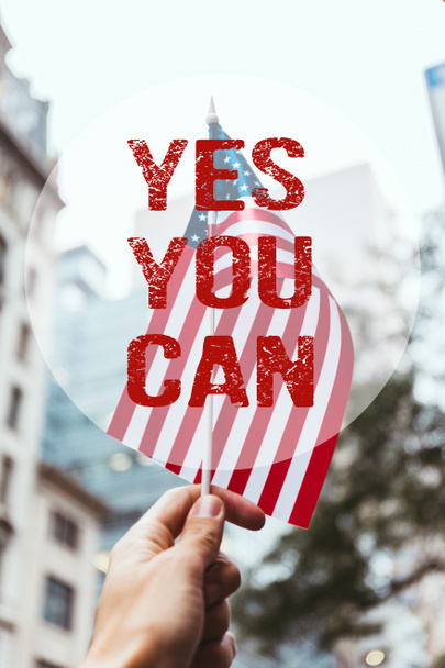 Schnappschuss eines Mannes mit amerikanischer Flagge in der Hand mit verschwommener New Yorker City Street im Hintergrund und "Yes you can" -Schriftzug - Foto, Bild