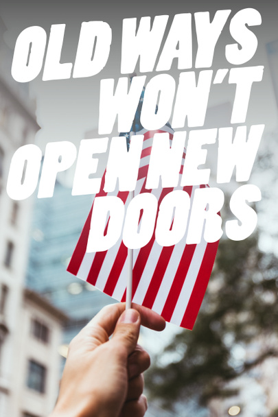 cropped shot of man holding american flag in hand with blurred new york city street on background and "old ways wont open new doors" quote - Fotó, kép