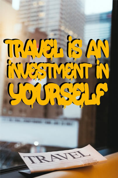 close up view of travel newspaper with "travel is an investment in yourself" quote on window and new york city on background - Photo, Image