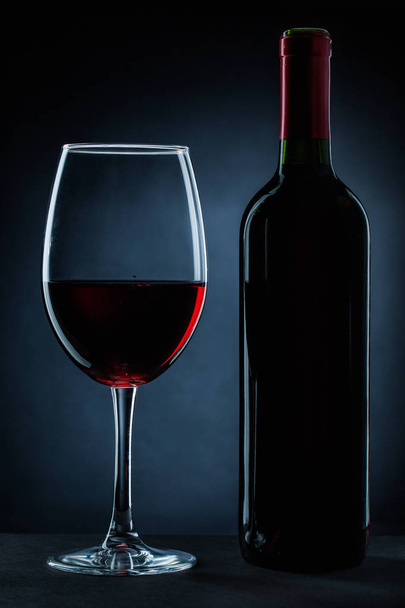 bottle and wineglass with red wine on black - Photo, image