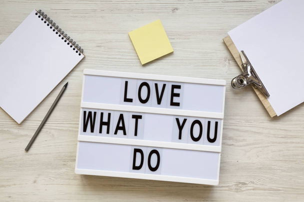 Modern board with text 'Love what you do', notepad, pencil and noticepad over white wooden background, top view. Business concept. From above, flat-lay, overhead.  - Photo, Image