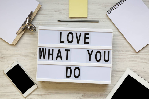 Modern board with text 'Love what you do', tablet, smartphone, notepad and pencil over white wooden background, top view. Business concept. From above, flat-lay, overhead.  - 写真・画像