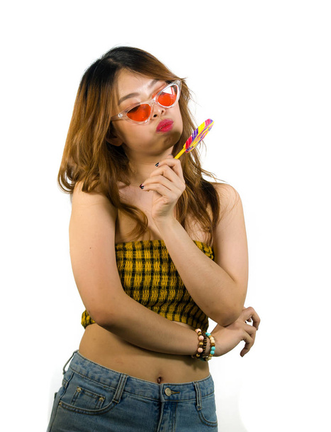 portrait of young happy and sexy Asian Korean girl in cool fashion sunglasses eating lollipop candy posing naughty teasing cheerful isolated on white background - Foto, afbeelding