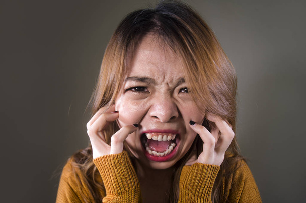 young crazy desperate and upset Asian Korean woman screaming scared and anxious feeling anger and pain isolated on dark background on dramatic pain face expression in depression concept - Foto, Bild