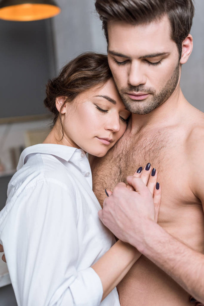 junges zartes Mädchen umarmt Mann sanft mit nacktem Oberkörper und geschlossenen Augen - Foto, Bild