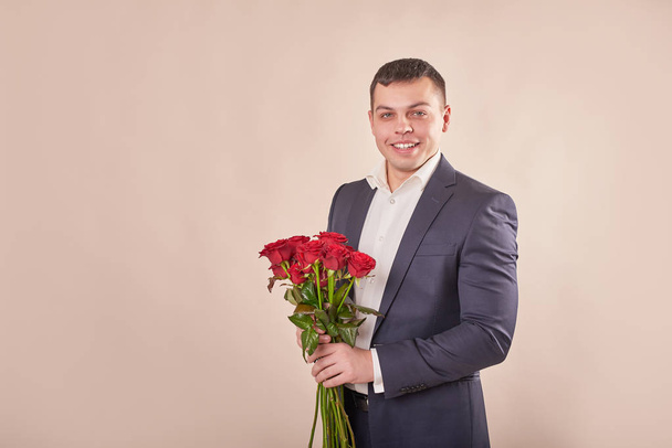 joven atractivo hombre con rosas rojas sobre un fondo beige en el Día de San Valentín 14 de febrero
 - Foto, imagen