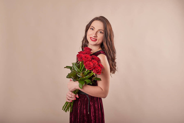 young attractive girl with red roses on a beige background on Valentine's Day February 14 - Zdjęcie, obraz