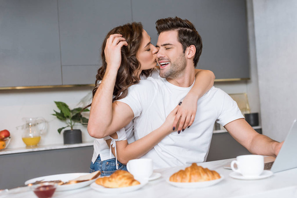 houkutteleva nainen syleilee ja suudella poski onnellinen mies lähellä aamiaista keittiössä
  - Valokuva, kuva