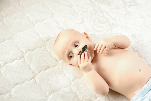 Kleine grappige jongen met kinderlijke tepel in de vorm van een snor. Grappige babyemoties. Babyverzorging Hygiëne. ruimte voor tekst. - Foto, afbeelding