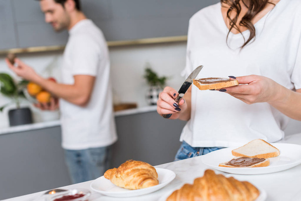 cropped view of toast bread and knife in hands of woman with boyfriend on background - Photo, Image