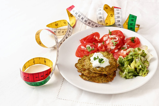 Brokkoli-Pfannkuchen mit Joghurt-Dip, Salat und Tomaten und Maßband, gesunde Schlankheitskost, weißer Teller auf weißer Tischdecke, ausgewählter Fokus, enge Schärfentiefe - Foto, Bild