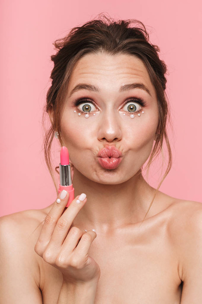 Image of a beautiful shocked happy young woman posing isolated over pink wall background holding lipstick. - Foto, imagen