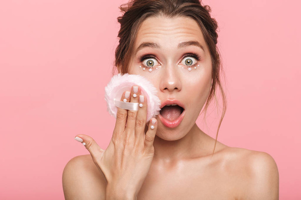 Image of a shocked young woman posing isolated over pink wall background holding powder puff. - Fotoğraf, Görsel